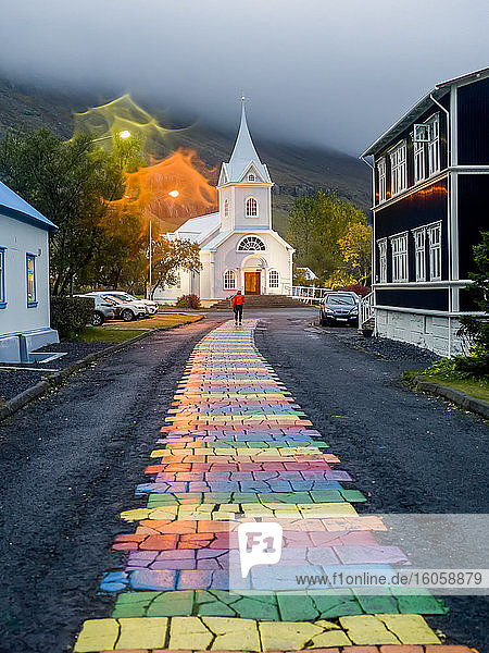 Bunter Weg inmitten einer asphaltierten Straße  der zu einer weißen Kirche führt; Seydisfjordur  östliche Region  Island