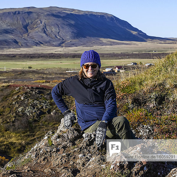 Frau sitzt auf einem Felsen und posiert für die Kamera  hinter ihr eine weite Landschaft Südislands; Grimsnes- og Grafningshreppur  Südliche Region  Island