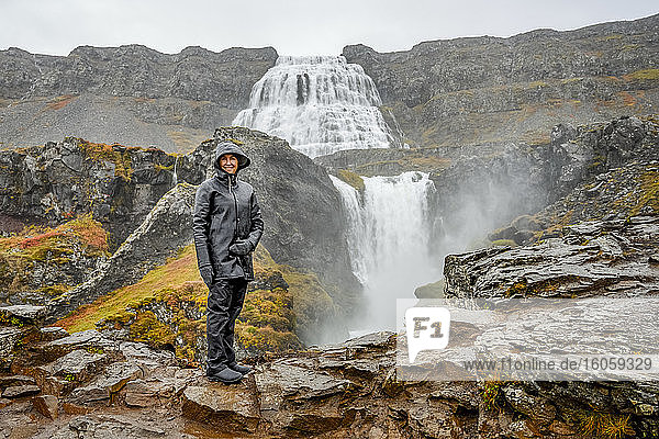 Eine Touristin steht auf einem Felsen bei Dynjandi (auch als Fjallfoss bekannt)  einer Reihe von Wasserfällen in den Westfjorden  Island. Die Wasserfälle haben eine Gesamthöhe von 100 Metern; Isafjardarbaer  Westfjorde  Island