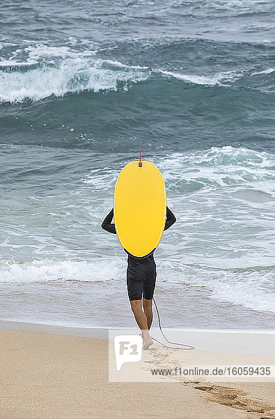 Ein männlicher Surfer geht am Strand mit einem leuchtend gelben Surfbrett in Richtung Wasser; Kihei  Maui  Hawaii  Vereinigte Staaten von Amerika
