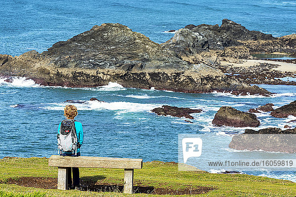 Eine Wanderin sitzt auf einer Holzbank mit Blick auf die felsige Küste; Grafschaft Cornwall  England