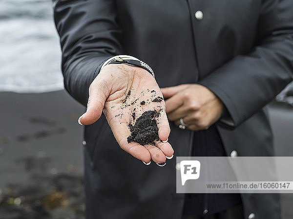 Eine Frau steht mit schwarzem Sand in der Hand; Island