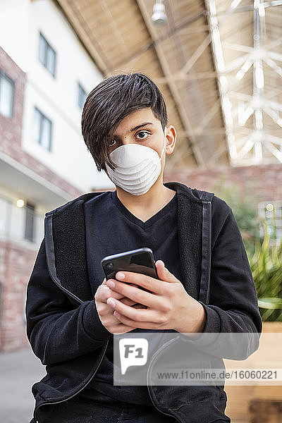 Zwischenmensch  der während der Coronavirus-Weltpandemie sein Smartphone benutzt und eine Schutzmaske zum Schutz vor COVID-19 trägt; Toronto  Ontario  Kanada