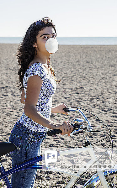 Portrait of a teenage girl standing with her bike and blowing a bubble with her bubblegum on Woodbine Beach; Toronto  Ontario  Canada