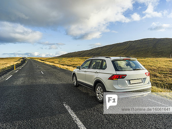 A vehicle is parked on the side of an asphalt road with a view of the vast landscape in Southern Iceland; Kjosarhreppur  Southern Region  Iceland