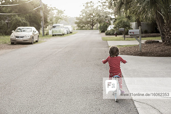 Ein fünfjähriger Junge im roten Hemd mit dem Fahrrad in einer ruhigen Wohnstraße.