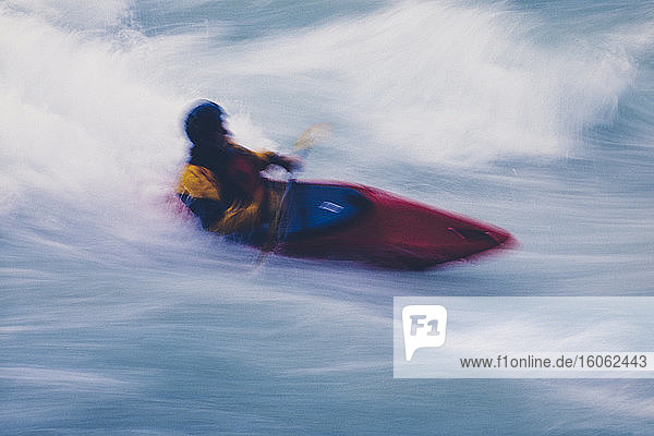 Long exposure of male whitewater kayaker paddling and surfing large rapids on a fast flowing river.