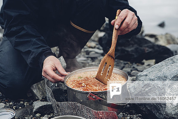 Ein wilder Camper  der in einem Topf heißes Essen umrührt und über einem Feuer kocht.