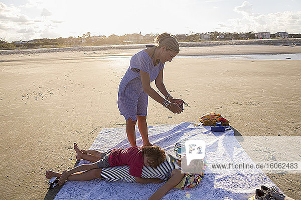 Mutter macht Smartphone-Foto von ihren Kindern am Strand bei Sonnenuntergang in Georgia