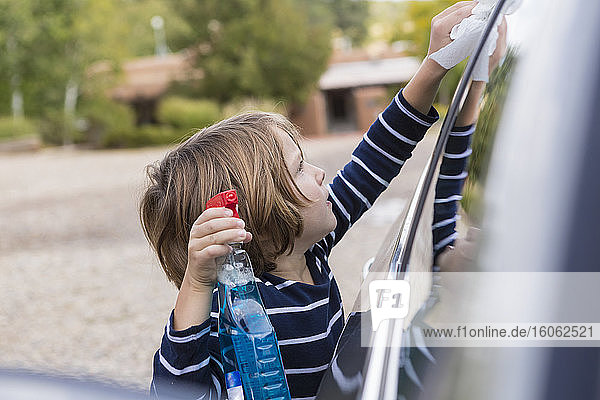 Vierjähriger Junge  der ein Auto außen mit Reiniger und einem Tuch poliert