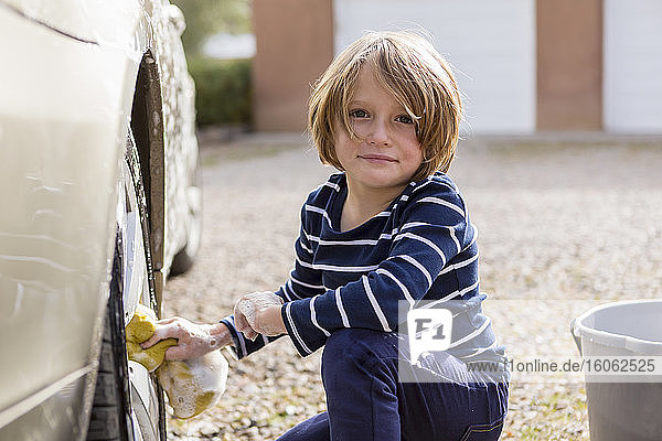 4 Jahre alter Junge  der auf dem Parkplatz ein Auto wäscht