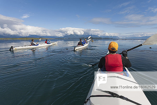A small group of people kayaks in pristine waters of an inlet on the Alaska coastline.