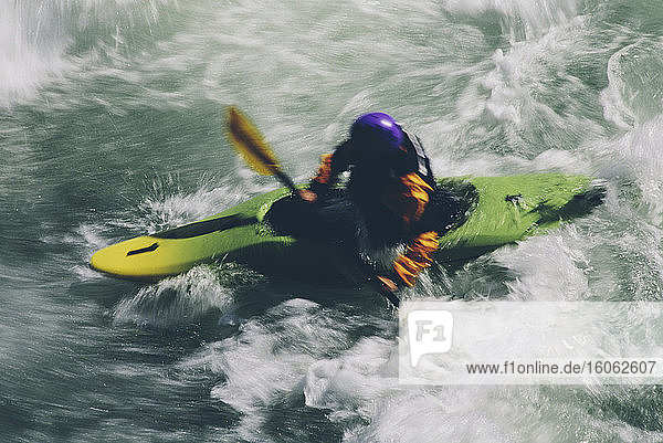 Whitewater kayaker paddles and surds large river rapids on a fast flowing river