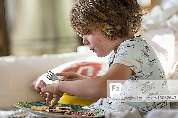4 Jahre alter Junge isst Pfannkuchen auf dem Sofa