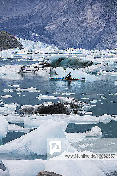 A sea kayaker paddling through ice in the lagoon at the terminus of the McBride Glacier.