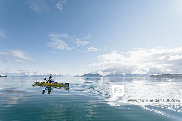 Mann Seekajakfahren an einem sonnigen Tag in einer Bucht an der Küste Alaskas.