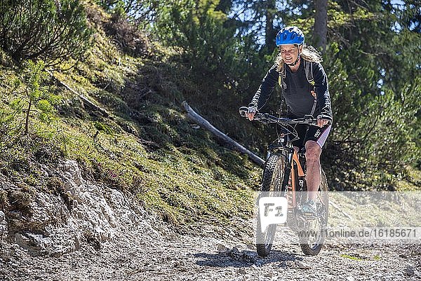 Female mountain biker rides with eMTB on a cart track uphill in the mountain forest  Rofan Mountains  Steinberg am Rofan  Tyrol  Austria  Europe