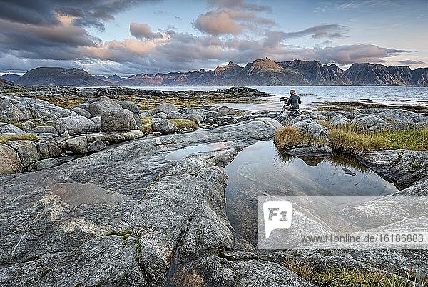 Kamerafrau filmt an Felsküste  hinten Meer und Lofotenberge  Gimsøy  Lofoten  Nordland  Norwegen  Europa