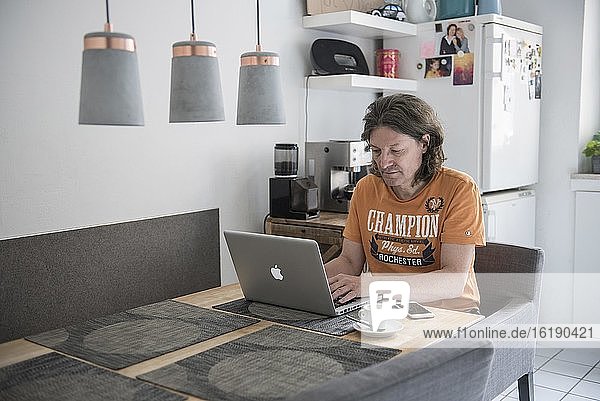Man in home office  works at kitchen table  laptop