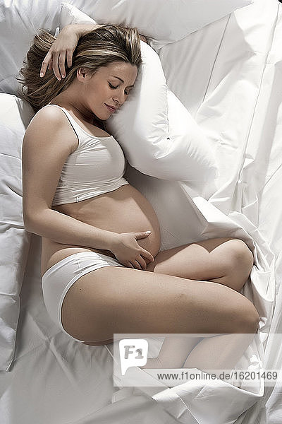 Portrait of heavily pregnant woman lying on bed  cradling stomach.