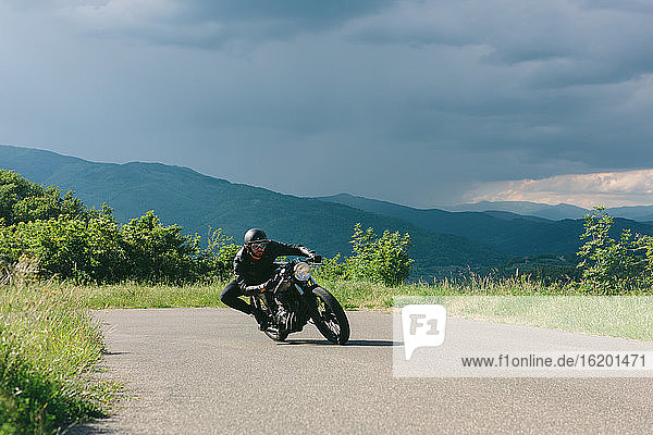 Young male motorcyclist on vintage motorcycle swerving around rural road bend  Florence  Tuscany  Italy