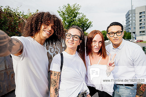 Mixed race group of friends hanging out together in town  taking selfie with mobile phone.