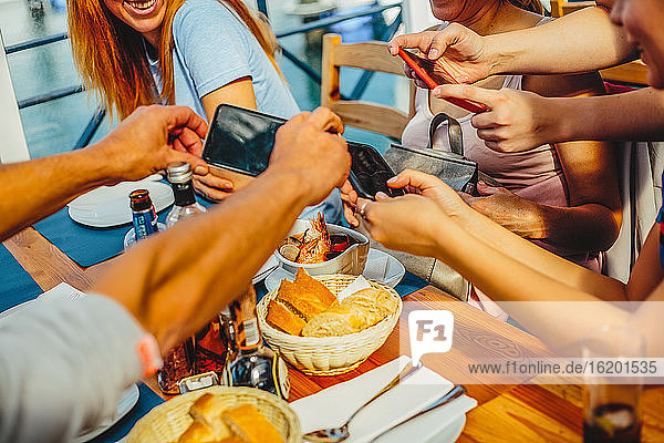 Eine Gruppe von Menschen sitzt an einem runden Tisch und macht mit Smartphones Fotos von Speisen