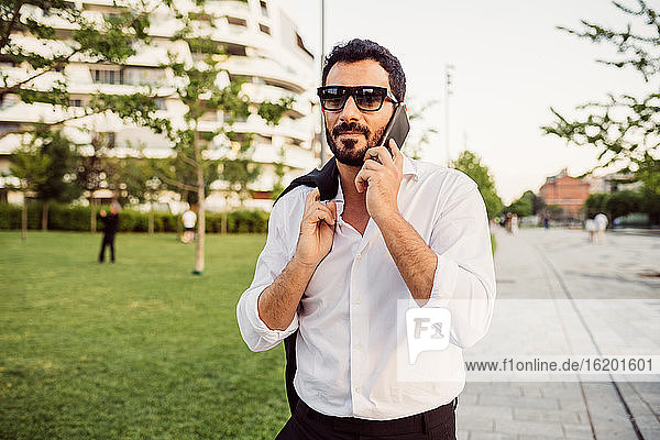 Portrait eines Geschäftsmannes mit weißem Hemd und Sonnenbrille  der ein Mobiltelefon benutzt.