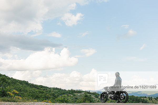 Junger männlicher Motorradfahrer auf einem Oldtimer-Motorrad mit Blick über die Landschaft  Florenz  Toskana  Italien