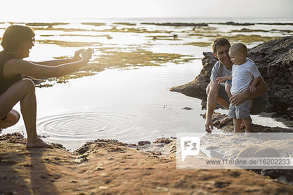 Mother taking photograph of father and son  on beach