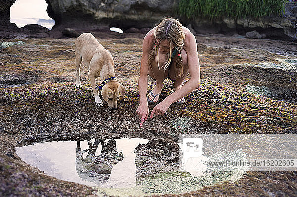 Frau schaut in ein Felsbecken  Hund neben ihr  Nusa Ceningan  Indonesien