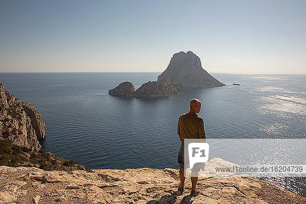 Mittlerer erwachsener männlicher Tourist  der von einer Klippe aus auf Es Vedra blickt  Ibiza  Spanien