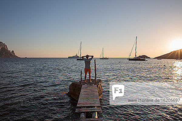 Junger Mann steht auf einem alten Pier bei Sonnenuntergang  Ibiza  Spanien