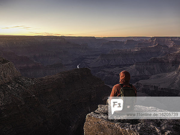 Man sitting on edge of South Rim  Grand Canyon National Park looking out at sunset  Arizona  USA