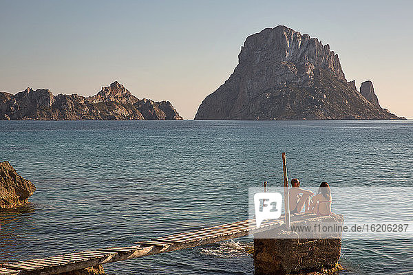 Touristenpaar auf dem Pier sitzend mit Blick auf Es Vedra  Ibiza  Spanien