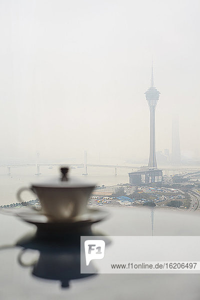 Teacup on table with misty view of river and Macau Tower, Macau