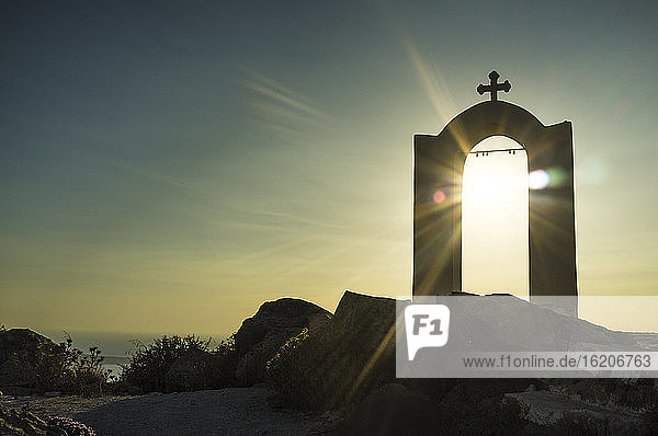 Blick auf einen religiösen Bogen und ein Kreuz bei Sonnenuntergang  Oia  Santorin  Griechenland