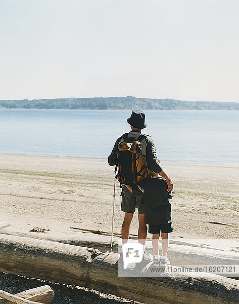 Vater und kleiner Sohn stehen Treibholzstamm und nehmen im Hinblick auf den Puget Sound