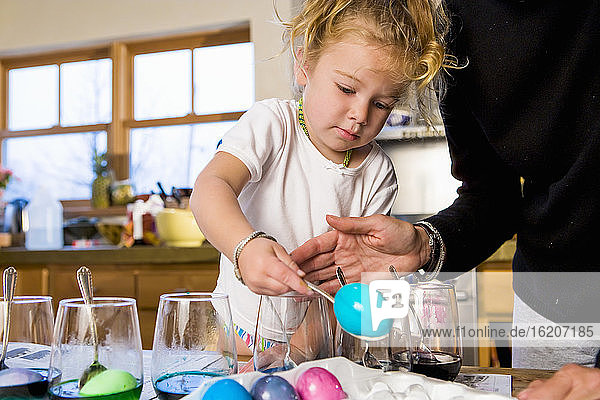 3-jähriges Mädchen  das zu Hause mit seiner Mutter Ostereier färbt