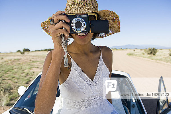 Ureinwohnerin Amerikas im Sonnenkleid sitzt auf weißem Cabrio-Sportwagen und macht Fotos