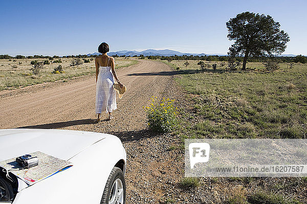 Ureinwohnerin Amerikas im Sonnenkleid fährt einen weißen Cabrio-Sportwagen auf Wüstensand