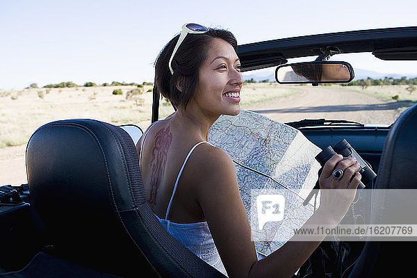 Native American woman in sun dress looking at a map in the passenger seat of a convertible.
