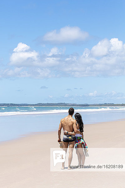 A good-looking Hispanic (Latin) couple on a deserted beach with backs to camera  Brazil  South America