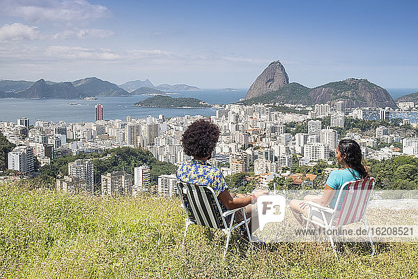 Ein multiethnisches Ehepaar sitzt zusammen und blickt auf den Zuckerhut und die Skyline von Rio  Rio de Janeiro  Brasilien  Südamerika