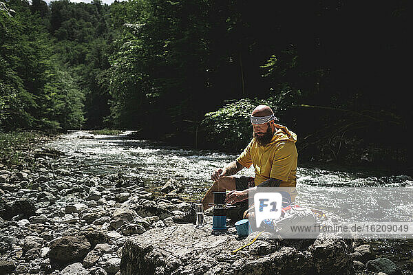 Hiker with full beard and yellow hoodie during break  cooking tea at riverside