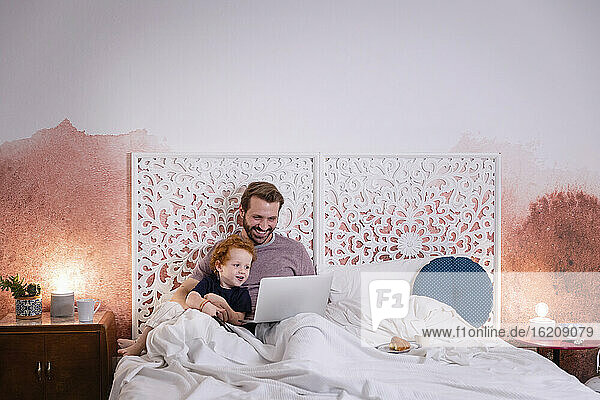 Lächelnder Vater mit süßem Sohn  der einen Laptop auf dem Bett zu Hause benutzt