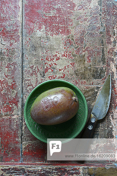 Kleine Schale  Mangofrucht und Küchenmesser liegen auf einer verwitterten Holzfläche