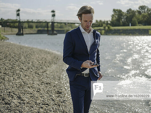 Geschäftsmann  der ein Mobiltelefon benutzt  während er am Flussufer steht  an einem sonnigen Tag
