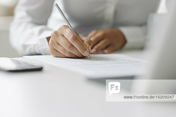 Nahaufnahme einer Geschäftsfrau  die am Schreibtisch im Büro zu Hause auf Papier schreibt