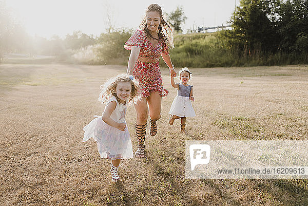 Glückliche Mutter läuft mit Töchtern auf einer Wiese im Gegenlicht